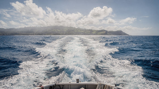 Trolling wake behind a boat in deep blue Hawaiian water with the Oahu coastline on the horizon